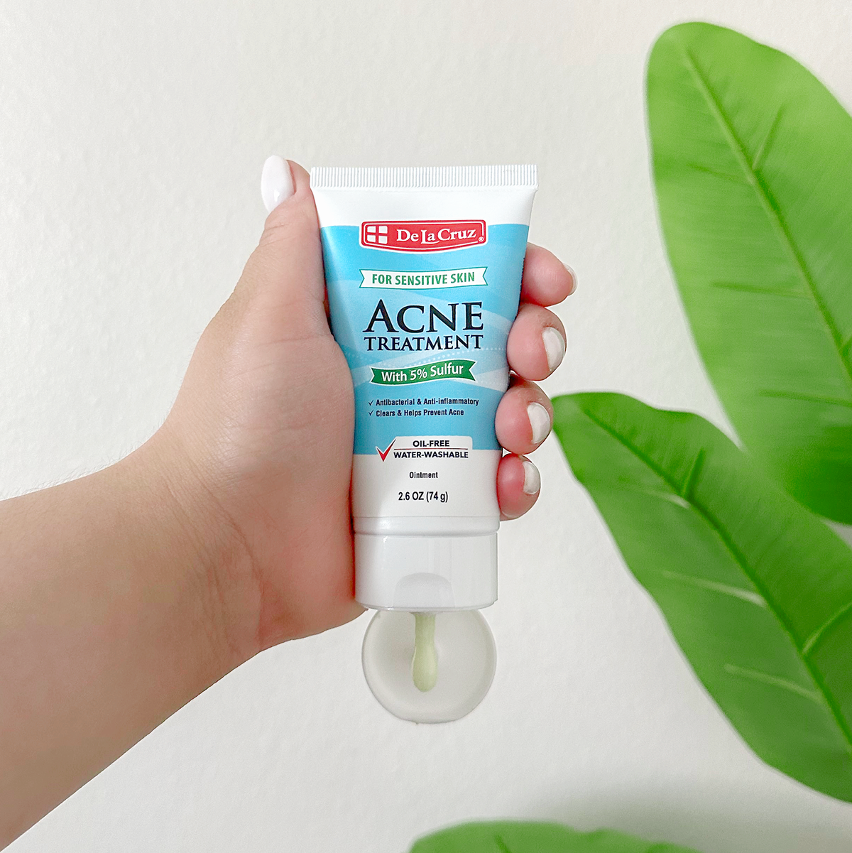 Hand holding tube of De La Cruz Acne Treatment with a some of the ointment dripping out of the tube. 