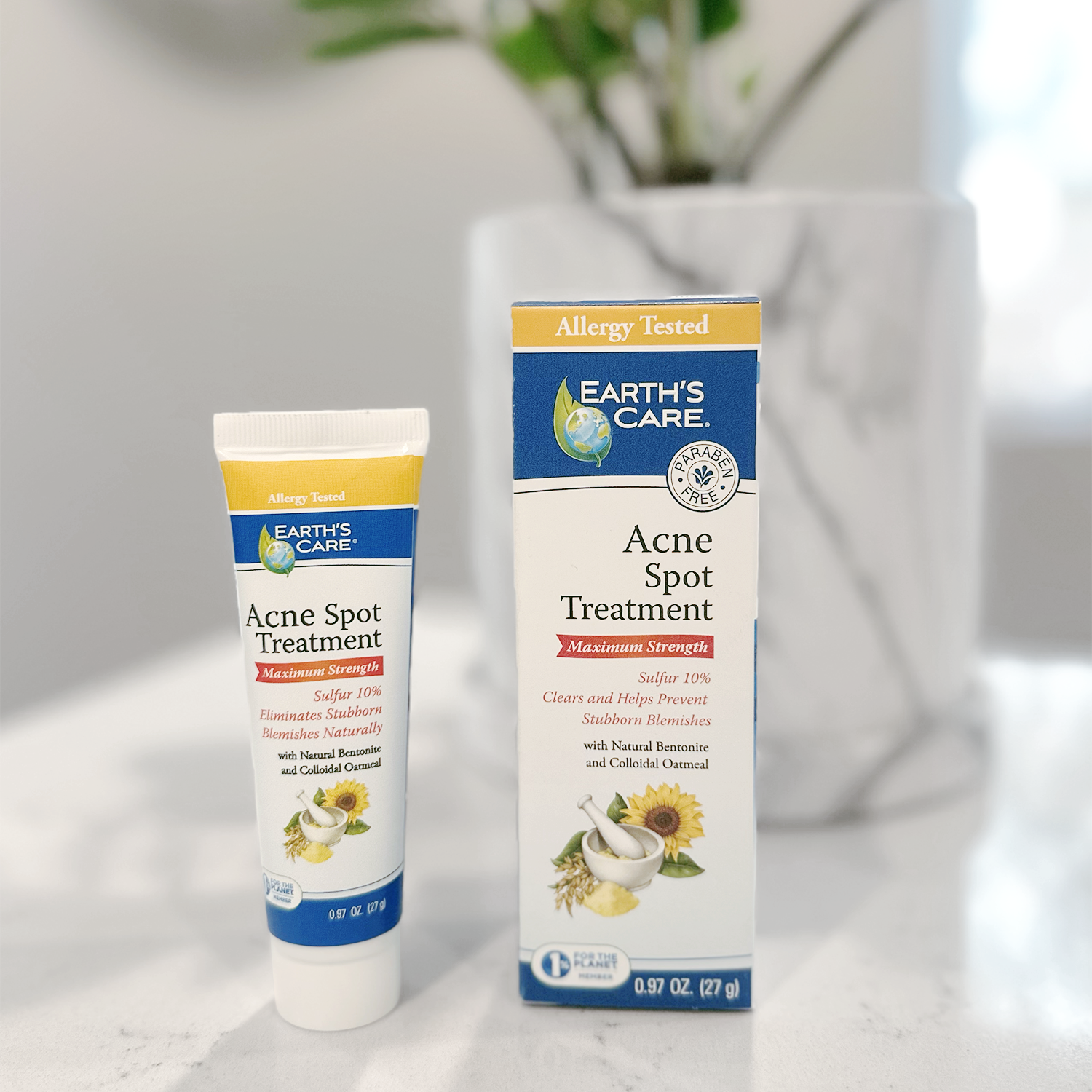 Earth's Care Acne Spot Treatment shown as a white squeeze tube and matching retail box on a light marble surface, with a softly blurred indoor background.