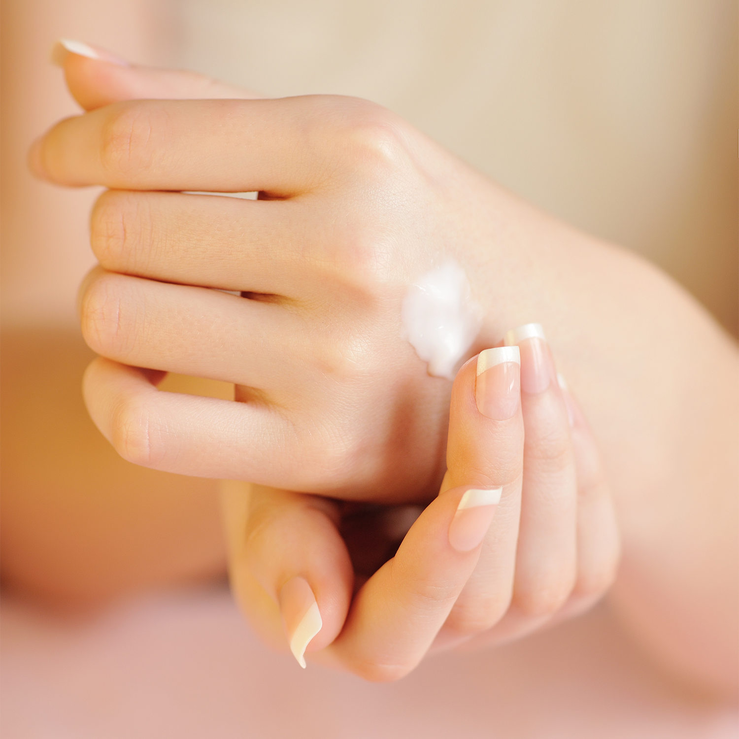 A close-up of a person's hands with a French manicure, one hand showing a dollop of shea butter on the back of the hand, against a soft, warm beige background.