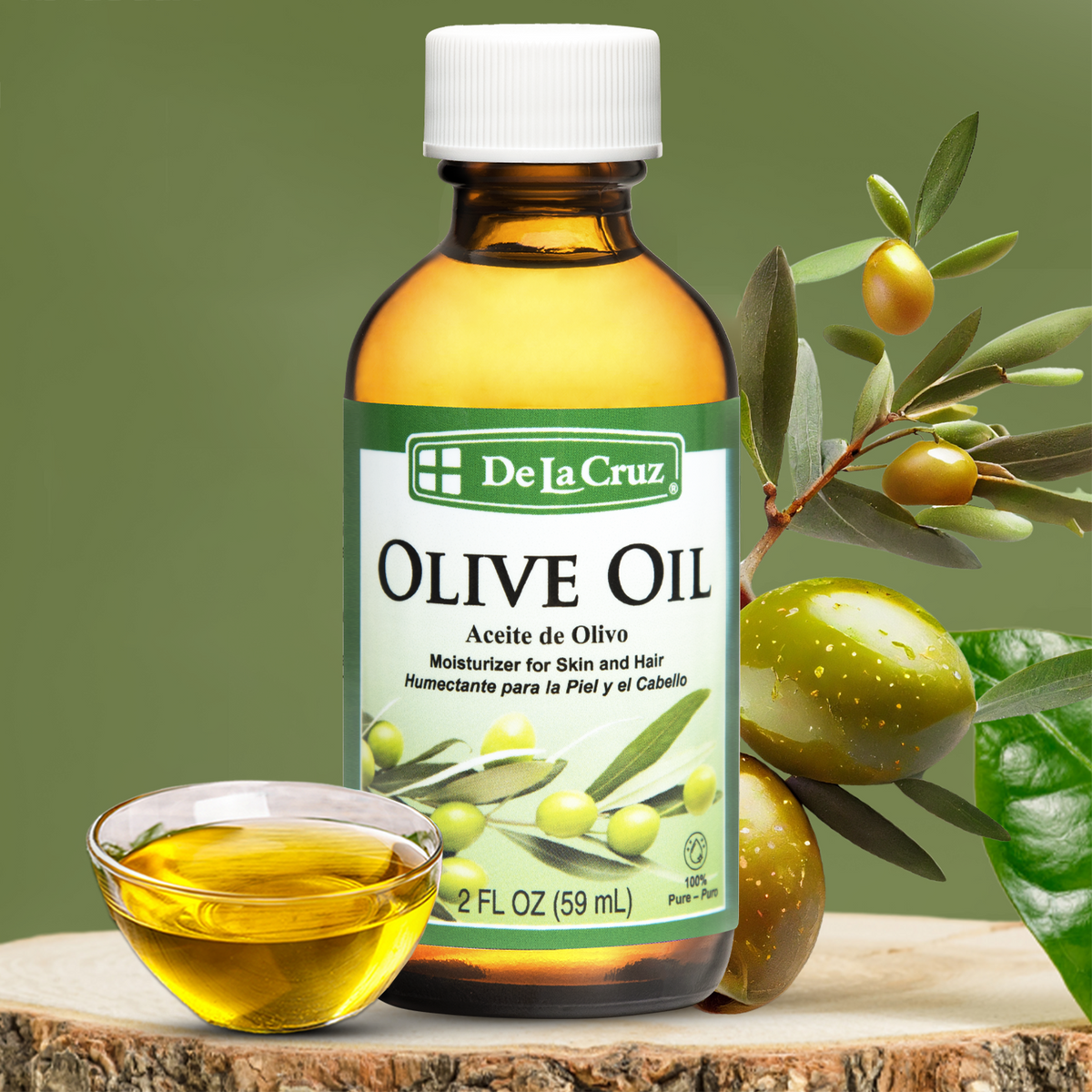 A bottle of De La Cruz Olive Oil with a small glass bowl of golden oil, set on a wood slice with olives and olive branches against a green background.