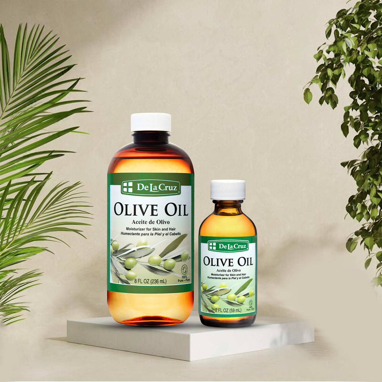 Two bottles of De La Cruz Olive Oil displayed on a white marble pedestal against a beige background, framed by green palm and leafy plants.