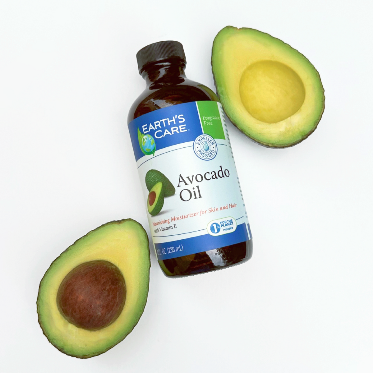 A bottle of Earth's Care Avocado Oil positioned between two halved avocados on a clean white background.