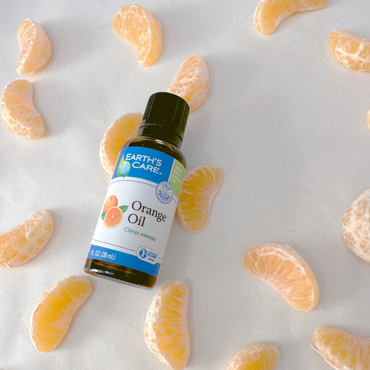 Earth's Care Orange Oil bottle surrounded by scattered peeled orange segments on a light neutral background.