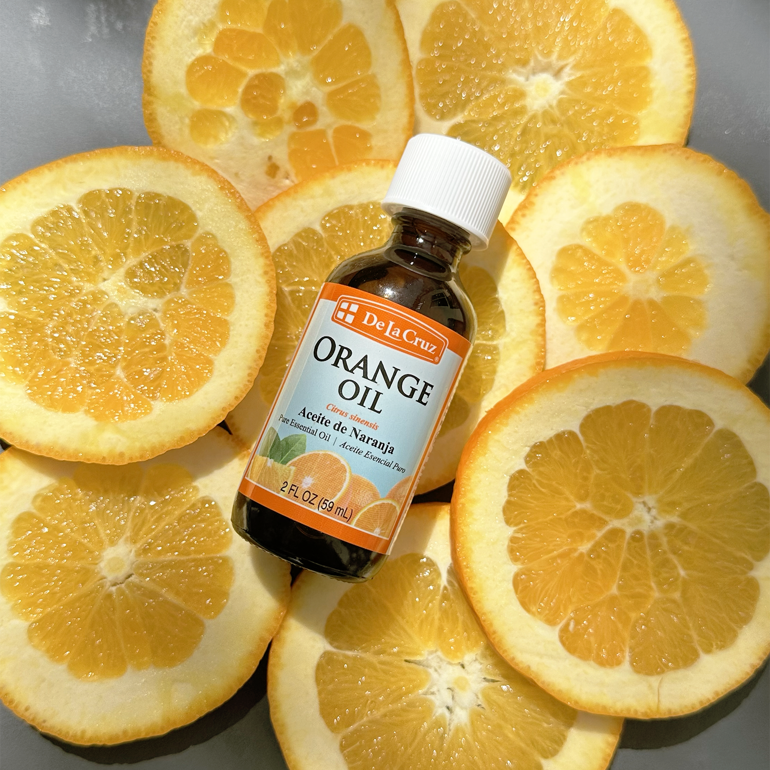 A bottle of De La Cruz Orange Oil placed on top of sliced orange halves, photographed from above on a gray surface.