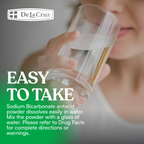 Person holding a glass of water with De La Cruz brand name and text about sodium bicarbonate antacid.