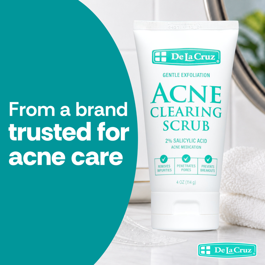 A white tube of De La Cruz Acne Clearing Scrub stands on a light marble surface with a folded white towel and a mirror in the background. A large teal graphic on the left reads, 'From a brand trusted for acne care.