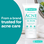 A white tube of De La Cruz Acne Clearing Scrub stands on a light marble surface with a folded white towel and a mirror in the background. A large teal graphic on the left reads, 'From a brand trusted for acne care.